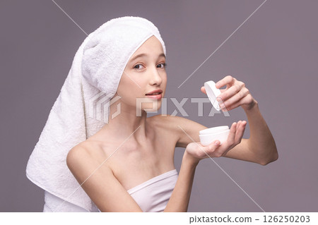 Young caucasian female applying skincare cream with towel on head in relaxed 126250203