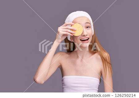 Young caucasian female skincare routine with cosmetic sponge and headband 126250214