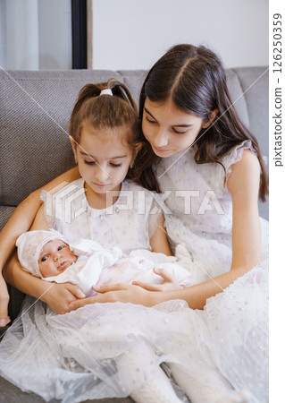 Newborn baby in the arms of his sisters in a white dress 126250359