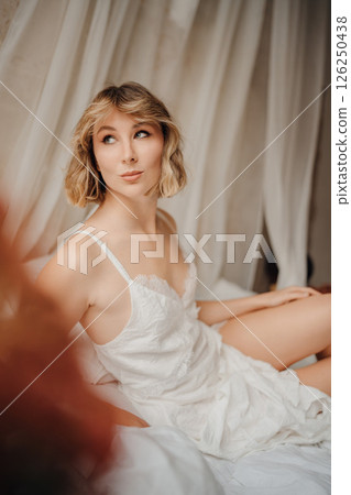 Beautiful young woman in a white dress on white sheets Beautiful young woman in a white dress on white sheets 126250438