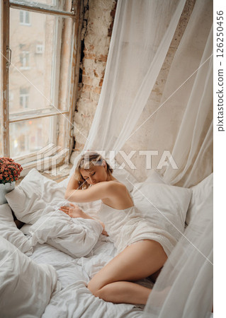 an attractive blonde woman in a white dress on white sheets an attractive blonde woman in a white dress on white sheets 126250456