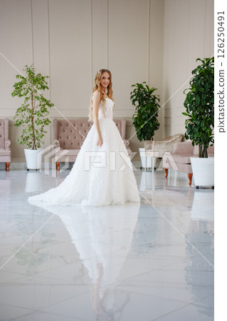 A bride with long blonde hair in a classic wedding dress in the living room.  126250491