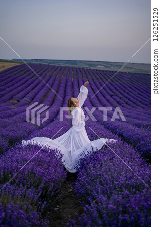 A woman in a white dress is standing in a field of purple flowers A woman in a white dress is standing in a field of purple flowers 126251529