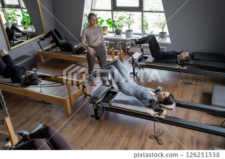 A group of woman exercises Glute bridge on a reformer bed machine in natural sunlight, focusing on pelvis and hips. A group of woman exercises Glute bridge on a reformer bed machine in natural sunlight, focusing on pelvis and hips. 126251538