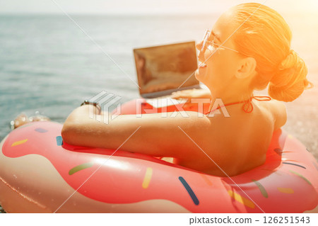 Woman laptop sea. Freelancer woman in sunglases floating on an inflatable big pink donut with a laptop in the sea. People summer vacation rest lifestyle concept 126251543