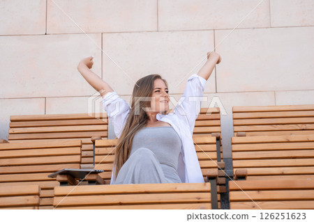 Woman, Bench, Joy - Smiling woman raising arms in celebration while sitting on wooden bench. 126251623