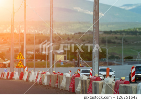 Red, white plastic safety barriers along road. Ensuring road safety with visible barriers. Effective safety measures for roadside work. Red, white plastic safety barriers along road. Ensuring road safety with visible barriers. Effective safety measures for roadside work. 126251642