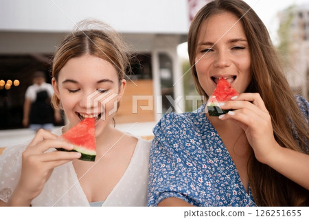 Watermelon Friends Summer Cafe: Two happy women enjoy refreshing watermelon slices at an outdoor cafe during summer. 126251655