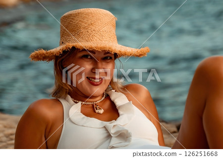 Woman Beach Sunbathing Summer - A woman in a white swimsuit relaxes on a rocky beach while wearing a straw hat, enjoying the summer sun. Woman Beach Sunbathing Summer - A woman in a white swimsuit relaxes on a rocky beach while wearing a straw hat, enjoying the summer sun. 126251668