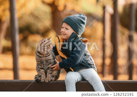 Young boy is sitting on the bench with cute cat outdoors Young boy is sitting on the bench with cute cat outdoors 126252191