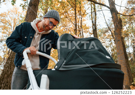 Looking inside the pram. Man is having a walk in the autumn park Looking inside the pram. Man is having a walk in the autumn park 126252223