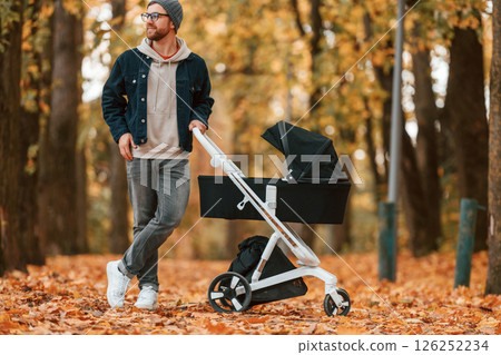 Standing and enjoying a nature. Man with pram is having a walk in the autumn park Standing and enjoying a nature. Man with pram is having a walk in the autumn park 126252234