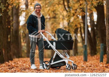 Standing and enjoying a nature. Man with pram is having a walk in the autumn park Standing and enjoying a nature. Man with pram is having a walk in the autumn park 126252237