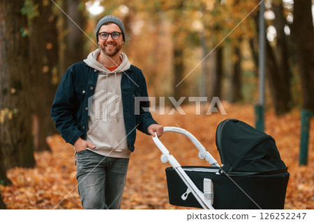 Front view. Man with pram is having a walk in the autumn park Front view. Man with pram is having a walk in the autumn park 126252247