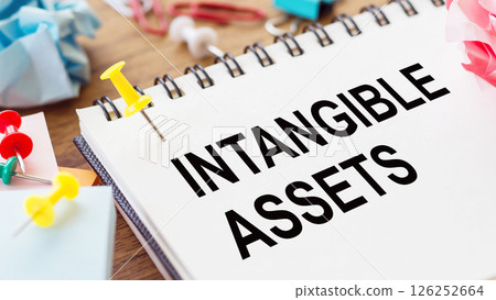 INTANGIBLE ASSETS - text on a notepad with wrinkled paper and paper needles on wooden background INTANGIBLE ASSETS - text on a notepad with wrinkled paper and paper needles on wooden background 126252664