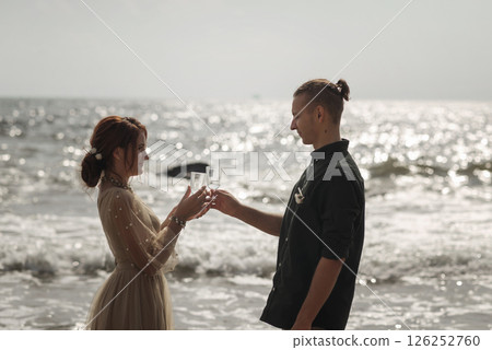 Romantic couple in love newlyweds standing on the sea background with glasses of champagne Romantic couple in love newlyweds standing on the sea background with glasses of champagne 126252760