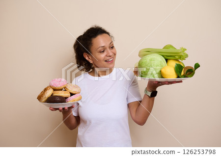 Healthy Lifestyle Choice Depicted by Woman Holding Plates of Fruits and Doughnuts Healthy Lifestyle Choice Depicted by Woman Holding Plates of Fruits and Doughnuts 126253798