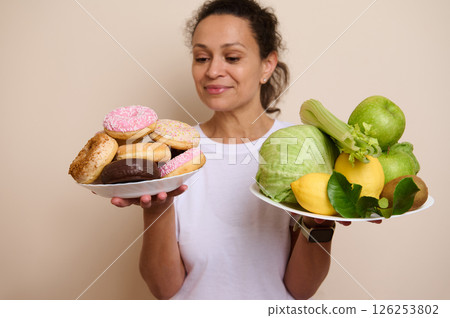 Balanced Choices: Woman Weighing Plates of Fresh Fruits and Sweet Doughnuts for Healthy Living 126253802