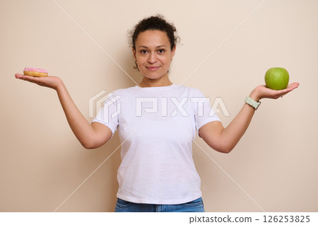 Smiling Woman Choosing Between a Healthy Green Apple and a Sugary Doughnut 126253825