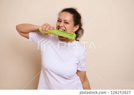 Woman Demonstrating Healthy Eating by Biting into a Fresh Celery Stalk in a Neutral Setting 126253827