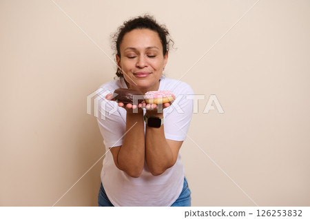 Smiling Woman Holding Two Doughnuts Reflecting on a Sweet Decision 126253832