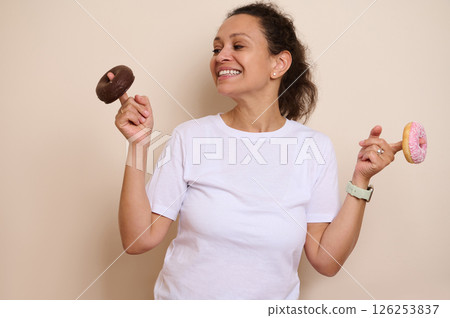 Joyful Woman Holding Two Vibrant Doughnuts, Smiling with an Enjoyable Expression 126253837