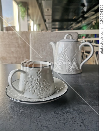 A white ceramic teacup with matching teapot on a modern table in a stylish cafe interior. 126254592