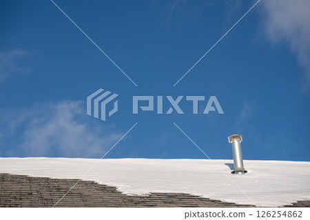 Snow and ice along a residential roof in the winter with a blue sky. 126254862