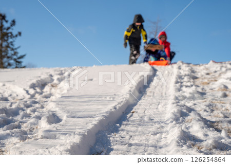 Selective focus on the snow path on the top of a hill with a child sledding down in a backyard  126254864