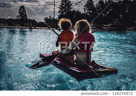 Two small kids paddling a cardboard boat in a race in a pool Two small kids paddling a cardboard boat in a race in a pool 126254872