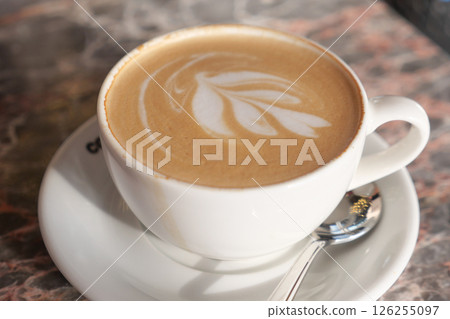 Warm latte with intricate foam design served in a cafe 126255097