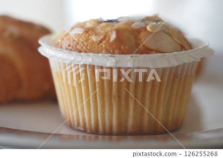 Muffin on a plate with croissants in a cozy bakery setting 126255268