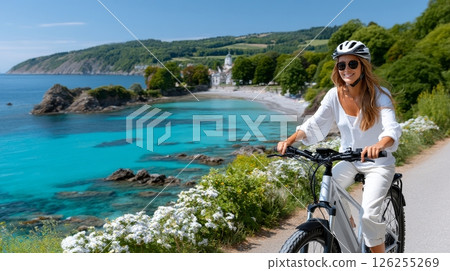 Caucasian female enjoying coastal bike ride by scenic beach and lush hills. 126255269