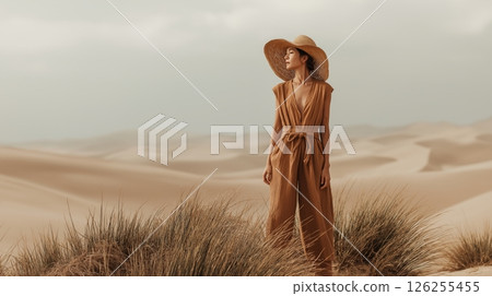 Caucasian female in desert wearing hat and jumpsuit amidst sand dunes. 126255455