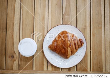 Croissant and coffee on a wooden table in a cozy cafe setting Croissant and coffee on a wooden table in a cozy cafe setting 126255467