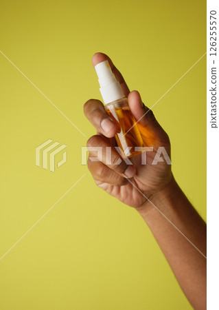 Hand holding a mouth wash spray bottle against a yellow background 126255570