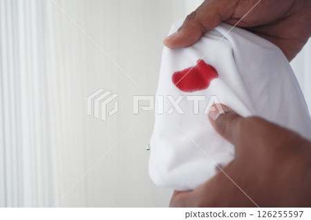 Red stain on white fabric being inspected closely by a hand 126255597