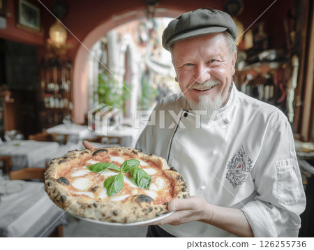 Italian restaurant atmosphere with smiling cheerful senior male chef holding pizza 126255736