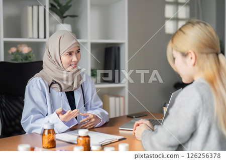 Compassionate Muslim female doctor discussing health concerns with a patient in her modern office, emphasizing healthcare support. Compassionate Muslim female doctor discussing health concerns with a patient in her modern office, emphasizing healthcare support. 126256378