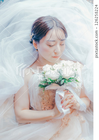 一位身穿純白色洋裝的女子躺著,胸前放著一束花束的圖片 一位身穿純白色洋裝的女子躺著,胸前放著一束花束的圖片 126258224