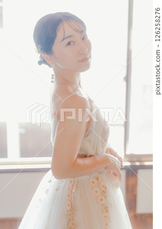 A woman in a white dress gazing at the camera in natural light A woman in a white dress gazing at the camera in natural light 126258276