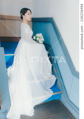 Portrait of a woman in a wedding dress sitting on the stairs and looking back Portrait of a woman in a wedding dress sitting on the stairs and looking back 126258494
