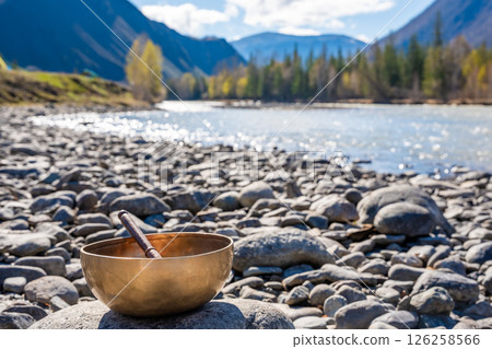 Tibetan singing bowl placed on river stones near mountain water in Altai. Concept of grounding energy, sacred silence, and spiritual resonance in wild nature Tibetan singing bowl placed on river stones near mountain water in Altai. Concept of grounding energy, sacred silence, and spiritual resonance in wild nature 126258566