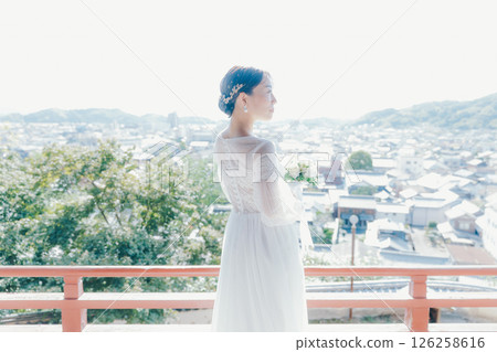 Portrait of a woman in a wedding dress looking out over the town from a shrine on a hill 126258616