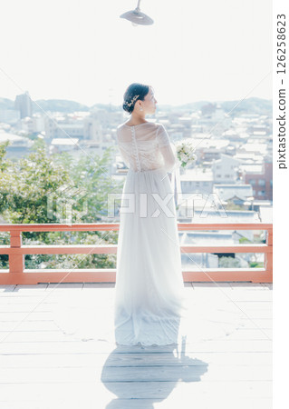 Portrait of a woman in a wedding dress looking out over the town from a shrine on a hill 126258623