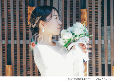 Portrait of a woman in a wedding dress standing against a background of Japanese decorations Portrait of a woman in a wedding dress standing against a background of Japanese decorations 126258709