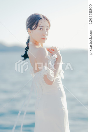 Portrait of a woman in a wedding dress standing in the backlight at the beach 126258800