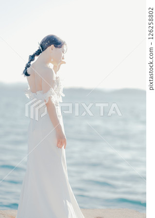 Portrait of a woman in a wedding dress standing in the backlight at the beach 126258802
