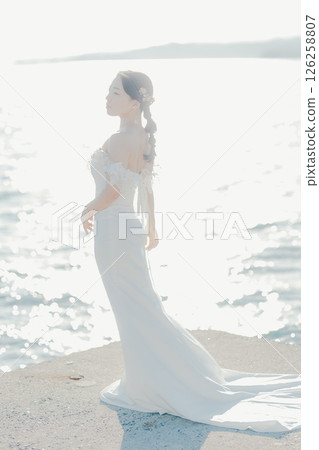 Portrait of a woman in a wedding dress standing in the backlight at the beach 126258807