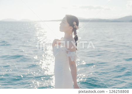 Portrait of a woman in a wedding dress standing in the backlight at the beach 126258808